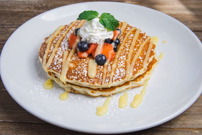 Pancakes topped with berries, whipped cream, and lemon drizzle